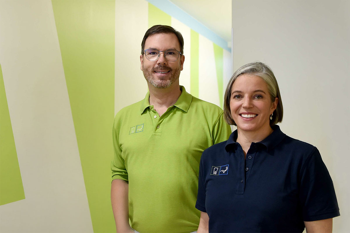 Dr. Andreas Hommens und Dr. Christiane Hommens stehen im grünen Flur ihrer Zahnarztpraxis